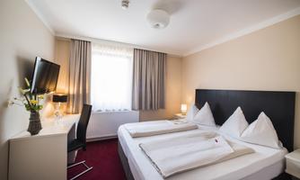 A cozy hotel room with a double bed and modern design. The room features a desk, a television, and plenty of natural light.
