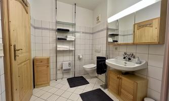 A modern bathroom with white tiles and wooden details. It includes a sink, a toilet, and a large mirror.