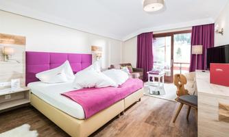 A modern hotel room with a cozy bed and purple curtains. There is a balcony with a view of the surroundings.