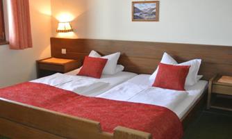 A cozy bedroom with a double bed and red pillows. A picture hangs on the wall, and there is warm light from a lamp.