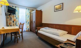A simple hotel room with a bed, a table, and a chair. The room has a television and a window with curtains.