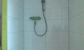 A modern shower with white tiles and a handheld showerhead. The room is bright and simply designed.