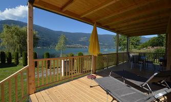 A terrace overlooking a beautiful lake and the surrounding mountains. There are lounge chairs and an umbrella that create a relaxed atmosphere.