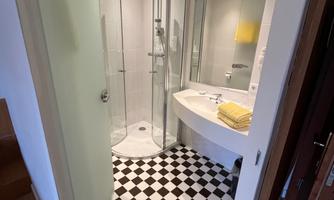 A modern bathroom with a shower area and an elegant washbasin. The floor features a classic black-and-white checkerboard pattern.
