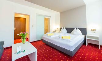 A modern hotel room with a double bed and two pillows. The room features a table with flowers and a cozy seating area.