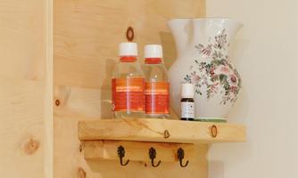 A wooden shelf with two bottles and a decorative jug. Below are three hooks attached.