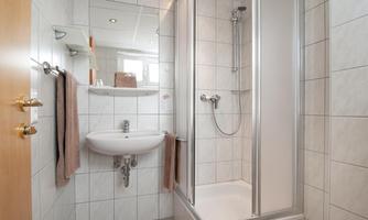 A modern bathroom with shower and sink. The walls are tiled with light tiles and there are towels available.