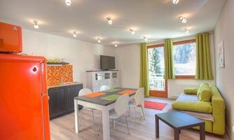 A modern kitchen with a red refrigerator and a dining area. The room has large windows with green curtains and a cozy seating area.
