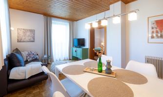 A modern living room with a dining area and a cozy couch. There are large windows that provide plenty of daylight.