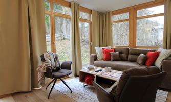 A cozy living room with large windows and plenty of natural light. The brown couch and the table create an inviting atmosphere.