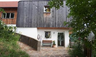 A modern house with a wooden wall and an inviting entrance area. Surrounded by plants and a paved path.