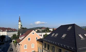 A city view with colorful houses and a building tower in the background. The sky is clear and blue.