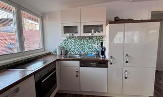 A modern kitchen with white cabinets and a colorful tiled backsplash. The equipment includes a stove, a dishwasher, and a refrigerator.