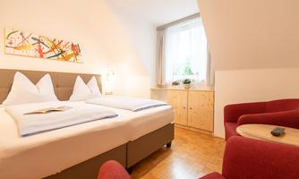 A cozy room with a double bed and red armchairs. Large window with natural light and modern decoration.