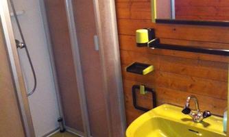 A bathroom with a yellow sink and a shower cubicle. The walls are made of wood, and there are basic sanitary facilities.