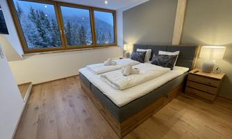 A modern bedroom with a large bed and cozy furnishings. Large windows provide a view of the snowy landscape.