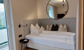 A stylish room with a modern bed and decorative pillows. A round mirror hangs on the wall and a small table complements the decor.
