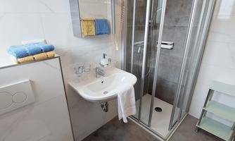 A modern bathroom with a glass shower and a sink. Towels in various colors are neatly arranged on the sink.