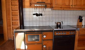 A rustic kitchen with wooden shelves and a stainless steel kitchenette. There is a stove, an oven, and cooking utensils hanging on the wall.
