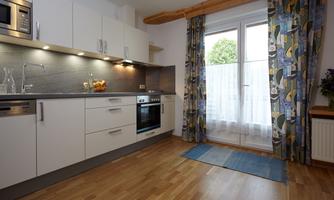 Modern kitchen with white furniture and wooden beams. Windows with curtains and a view outside.