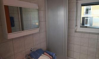 A small bathroom with a sink, a mirror, and a shower cabin. The tiles are designed in light colors and the window provides daylight.