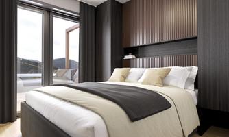 A modern bedroom with a large bed and elegant furnishings. Large windows offer a view of the surroundings and let in plenty of light.