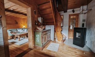 A cozy wooden house with a wooden staircase, a typical stove, and a seating area. The walls and furniture are made of wood and create a warm atmosphere.