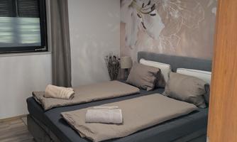 A modern bedroom with a double bed and neutral bedding. There is a floral pattern on the wall and the light is soft.