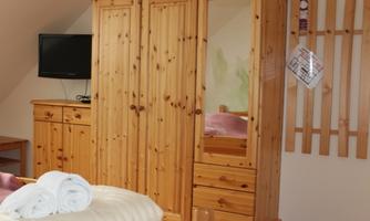 A cozy room with a wooden wardrobe and a small table. Towels are laid out on the bed, and a television is mounted on the wall.