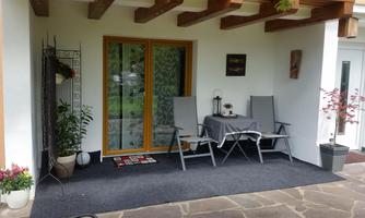 An inviting outdoor area with a table and two chairs. The door is made of glass and there are plants for additional decoration.