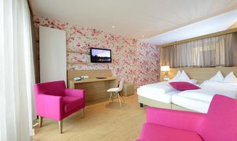 A modern hotel room with a blooming, floral-decorated background. There are two beds, a television, and pink chairs.