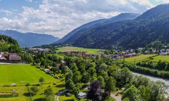 A picturesque landscape with hills, a tranquil river, and a small village. The sky is blue with some clouds.