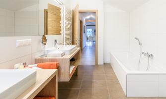 A modern bathroom with bright tiles and wood details. There is a bathtub, two sinks, and plenty of light.