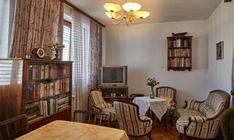 A cozy living room with bookshelves and a table. The windows let in a lot of light and the furniture is in a classic style.
