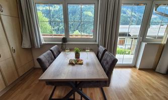 A modern dining area with a wooden tray and comfortable chairs. Through the windows, there is a beautiful view of the mountains.