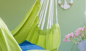 A green hammock hangs on a wall with maritime decoration. Next to the hammock, there are flowers in a pot and an anchor symbol.