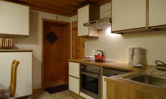 A modern kitchen with wooden shelves and white furniture. The room has a warm, inviting atmosphere.