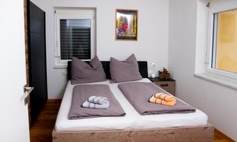 A cozy bedroom with a large bed and two pillows. A colorful picture hangs on the wall, and fresh towels are ready.