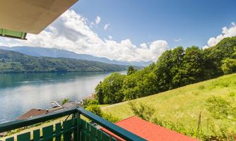 A beautiful view of a lake surrounded by mountains and trees. The sky is blue with some clouds.
