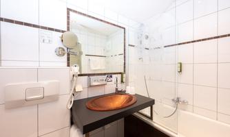 A modern bathroom with an elegant washbasin and a bathtub. White tiles and a large mirror create a bright atmosphere.
