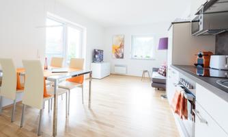 A bright kitchen with a dining area and modern furniture. White walls and large windows create a lot of light in the room.