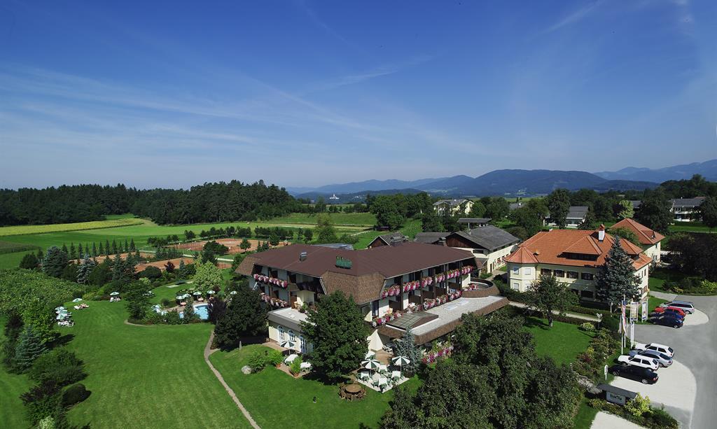 A picturesque country hotel surrounded by green meadows and trees. The landscape offers a tranquil atmosphere and a beautiful view of the mountains in the background.