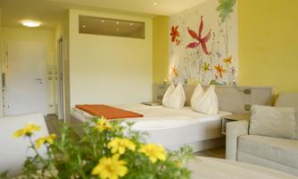A bright room with a large bed and a cozy sofa. The walls are decorated with colorful flower patterns.
