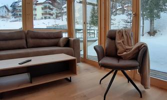 A cozy living area with a sofa and an armchair. Outside, snow lies on the ground, and the view is visible through large windows.