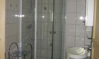 A modern bathroom with a shower, sink, and wooden details. The walls are light tiled and the floor is dark.