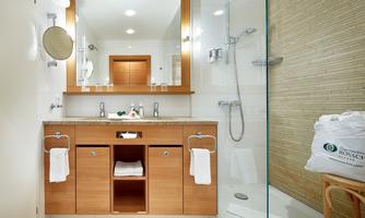 A modern bathroom with wooden furniture under the sink. There is a shower with a glass wall and a large mirror.