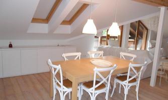 A modern dining room with a large wooden table and white chairs. The skylights provide plenty of daylight.