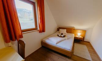 A simple room with a single bed and orange curtains. Next to the bed, there is a nightstand with a lamp and a small carpet on the floor.