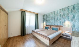 A modern bedroom with two single beds and a stylish wallpaper. Large windows let in plenty of light and create an inviting atmosphere.