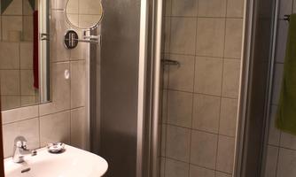 A small bathroom with a shower cubicle and a sink. The walls are tiled with light tiles and there is a mirror.